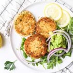 A plate with canned salmon patties, shown served over greens with avocado and onions.