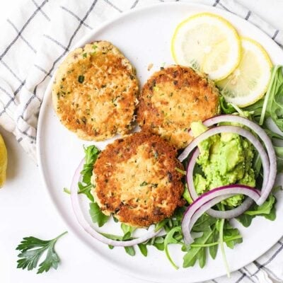 A plate with canned salmon patties, shown served over greens with avocado and onions.