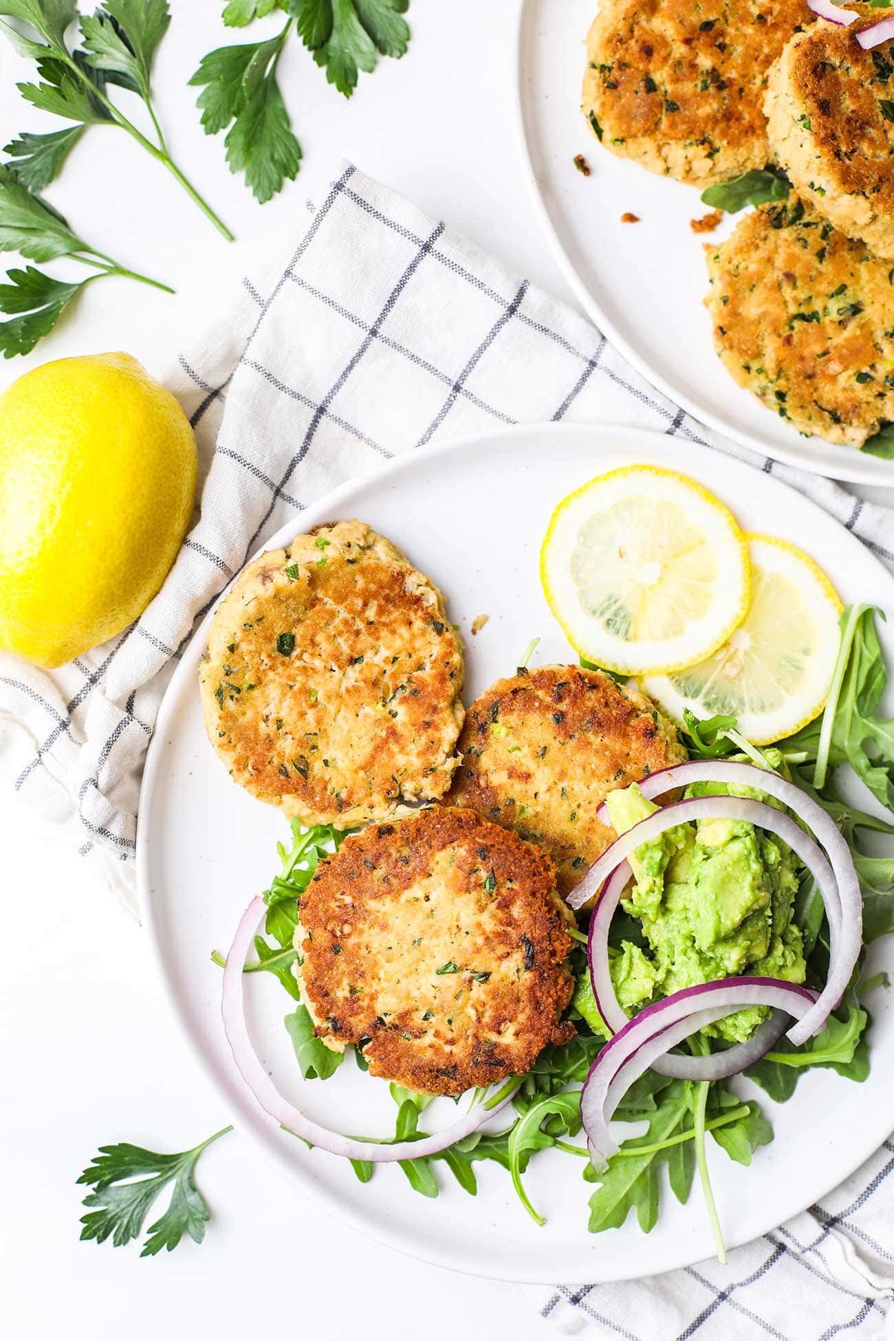 A plate with 3 crispy browned canned salmon patties on top of an arugula salad.