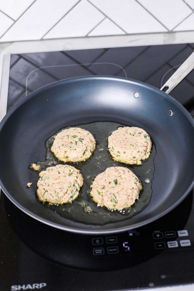 4 salmon patties shown cooking in olive oil.