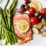 A white plate shown with salmon, asparagus, potatoes, tomatoes, and olives.