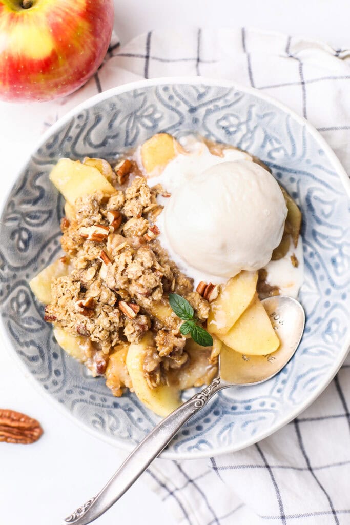 A bowl with gluten free apple crisp topped with melty vanilla ice cream.