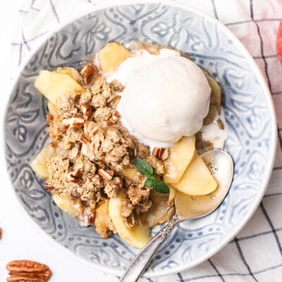 A bowl of gluten free apple crisp with a melted scoop of ice cream.