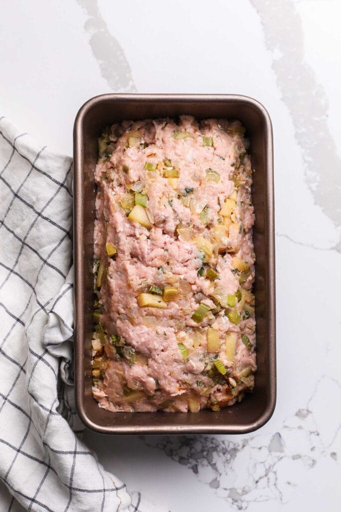 Ground chicken with vegetables pressed into a loaf pan.